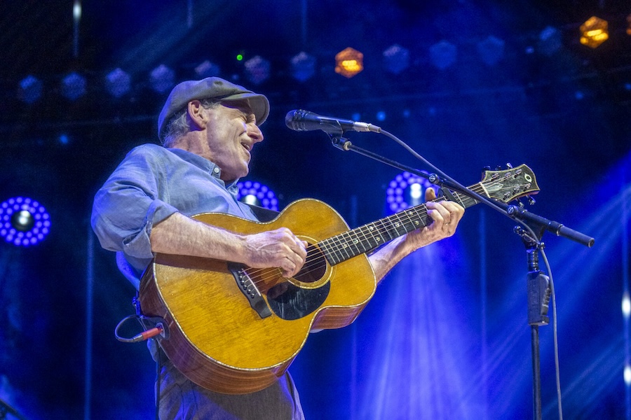 James Taylor sings and plays guitar under bright stage lights in a live performance.