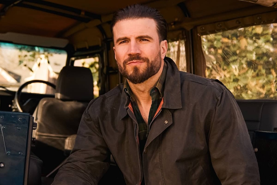 Sam Hunt poses inside a rugged vehicle with a confident expression and trimmed beard.