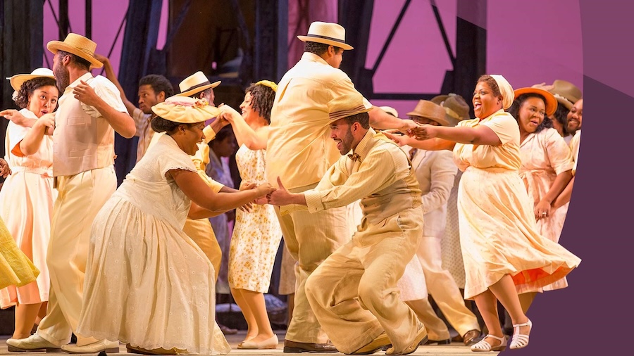 Performers in pastel costumes dance joyfully during a scene from Porgy and Bess.