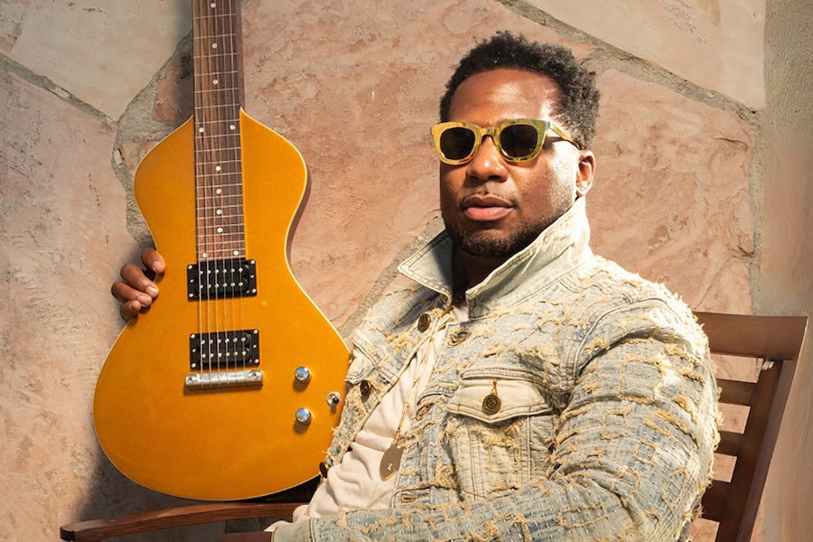 Musician Robert Randolph poses with a gold electric guitar and wears yellow sunglasses.